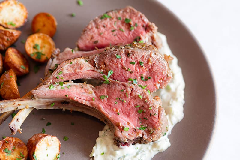 A closeup shot of Whole30 rack of lamb with dairy-free Tzatziki Sauce.