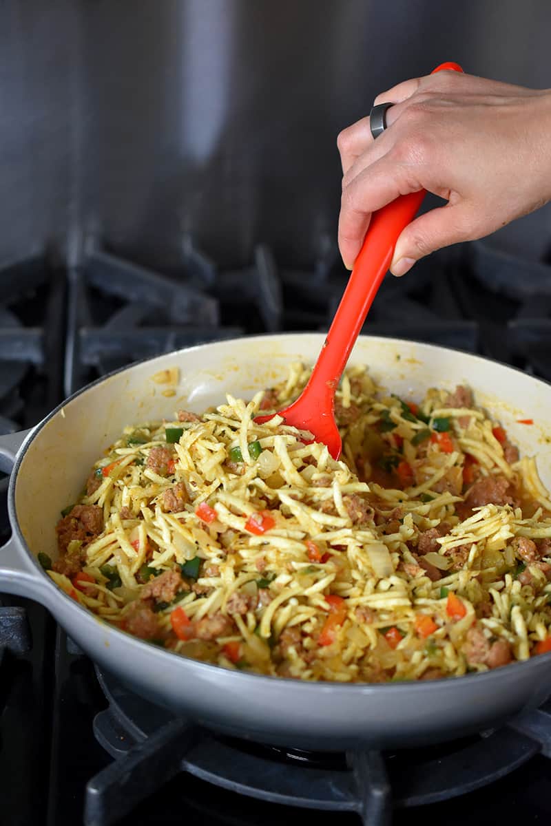 A red silicone spatula is mixing the filling for paleo and Whole30 Mexican breakfast casserole in a gray enameled cast iron skillet
