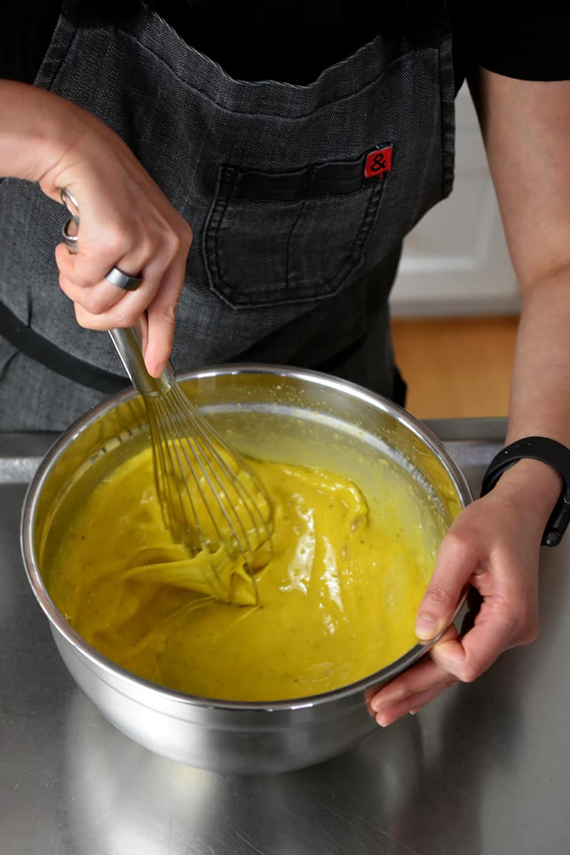 Overhead shot of someone in a gray apron whisking the eggs for a low carb Mexican Breakfast Casserole