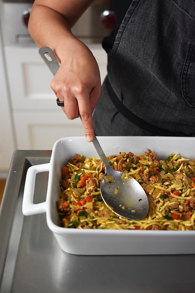 Someone using the back of large spoon to smooth out the filling for Mexican Breakfast Casserole