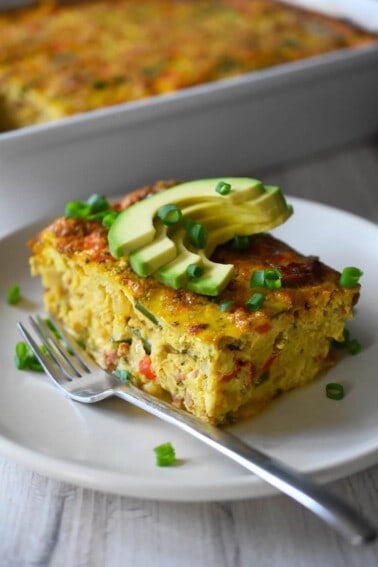A slice of Mexican Breakfast casserole is on a plate in front of a casserole pan.