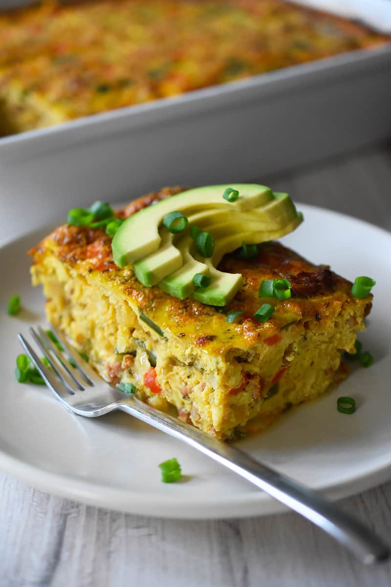 A slice of Mexican Breakfast casserole is on a plate in front of a casserole pan.