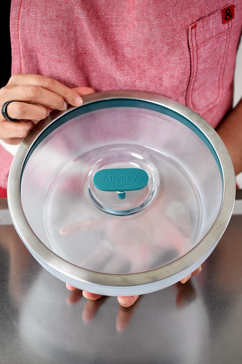 Someone in a red apron is holding a round Anyday microwave glass container.