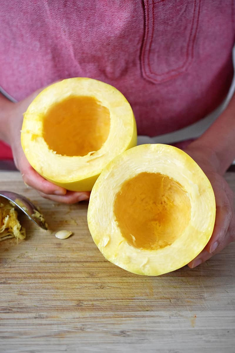 A spaghetti squash is cut in half crosswise and the seeds have been scooped out and discarded