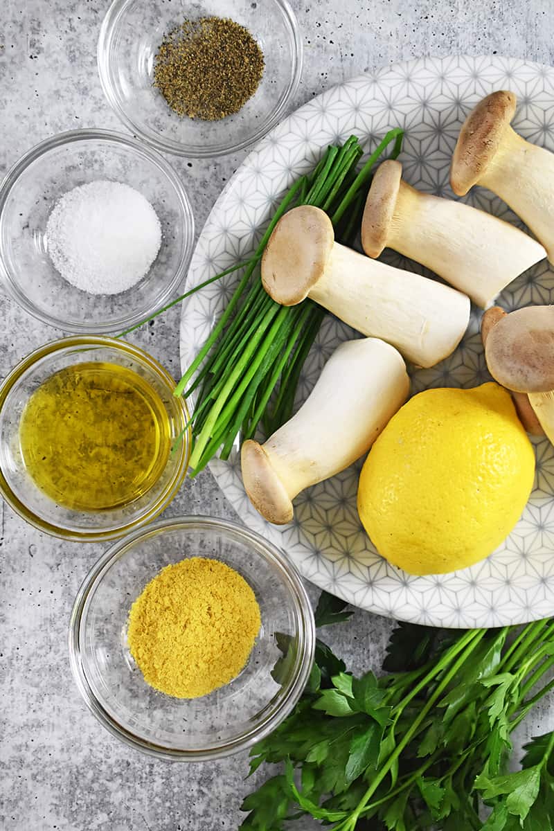 An overhead shot of the ingredients for king oyster mushroom salad: mushrooms, lemon, nutritional yeast, extra virgin olive oil, and salt.