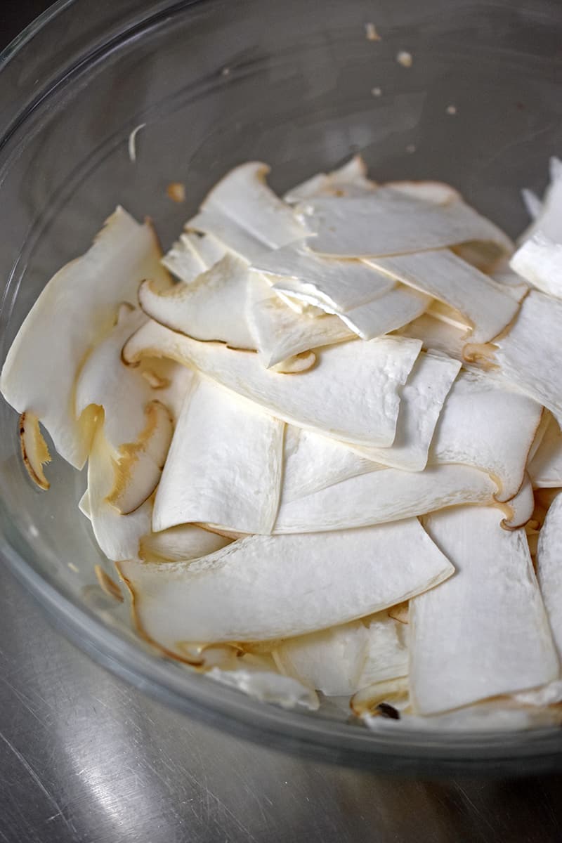 Close up of thinly sliced king oyster mushrooms in a glass bowl.