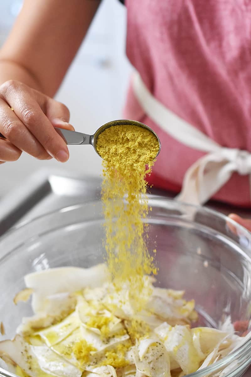 Pouring a tablespoon of nutritional yeast into a bowl of shaved mushroom salad.