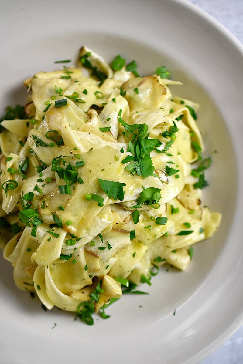 An overhead shot of a platter of shaved and raw king oyster mushroom salad with lemon, olive oil, and herbs.