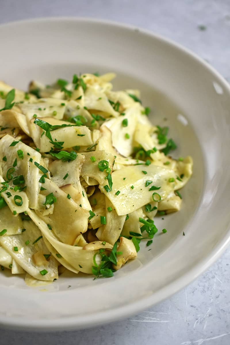 Closeup side angle of a bowl of King Oyster mushroom salad with lemon vinaigrette and fresh herbs