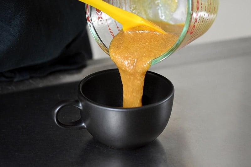 Pouring pumpkin mug cake into a black coffee mug.