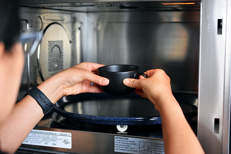 Someone placing a black coffee mug filled with pumpkin mug cake batter in the center of the microwave.