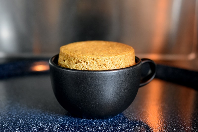 A pumpkin mug cake that is golden brown inside a black coffee mug.