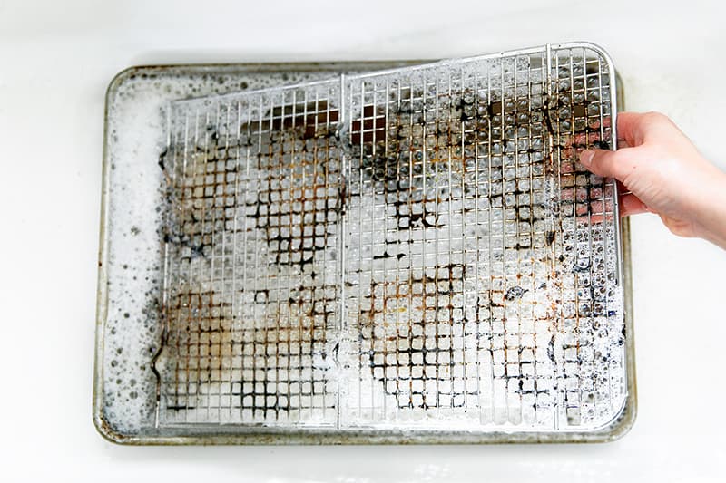 Soaking a dirty wire rack in hot soapy water to clean it.