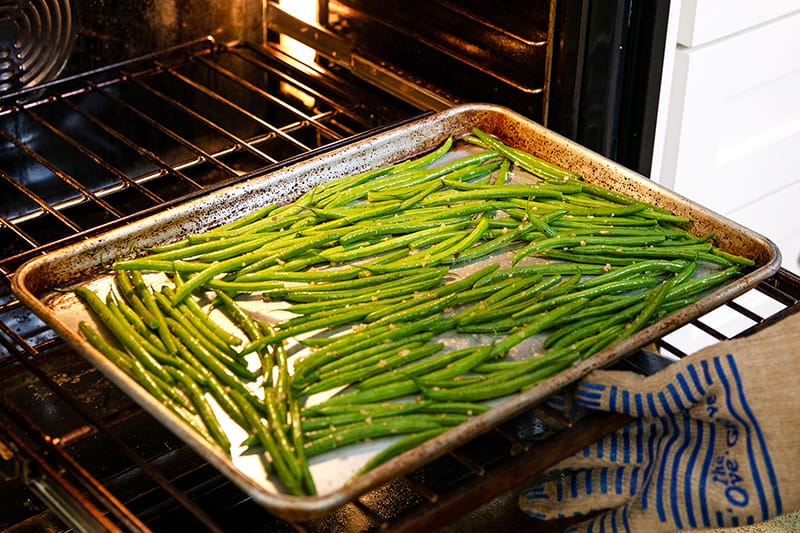 Putting a rimmed baking sheet with green beans into an oven.