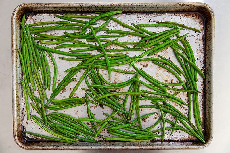An overhead shot of a rimmed baking sheet with roasted green beans with lemon and garlic.
