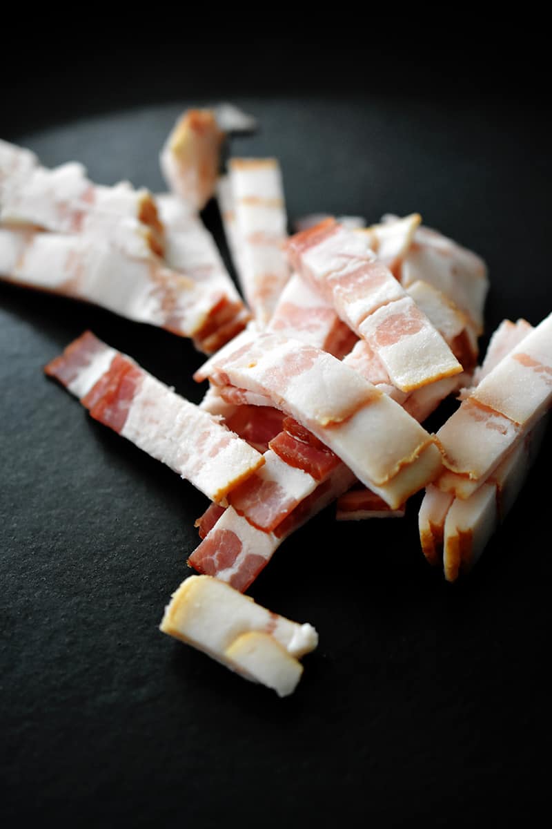 Close up of raw bacon pieces in a cold cast iron skillet.