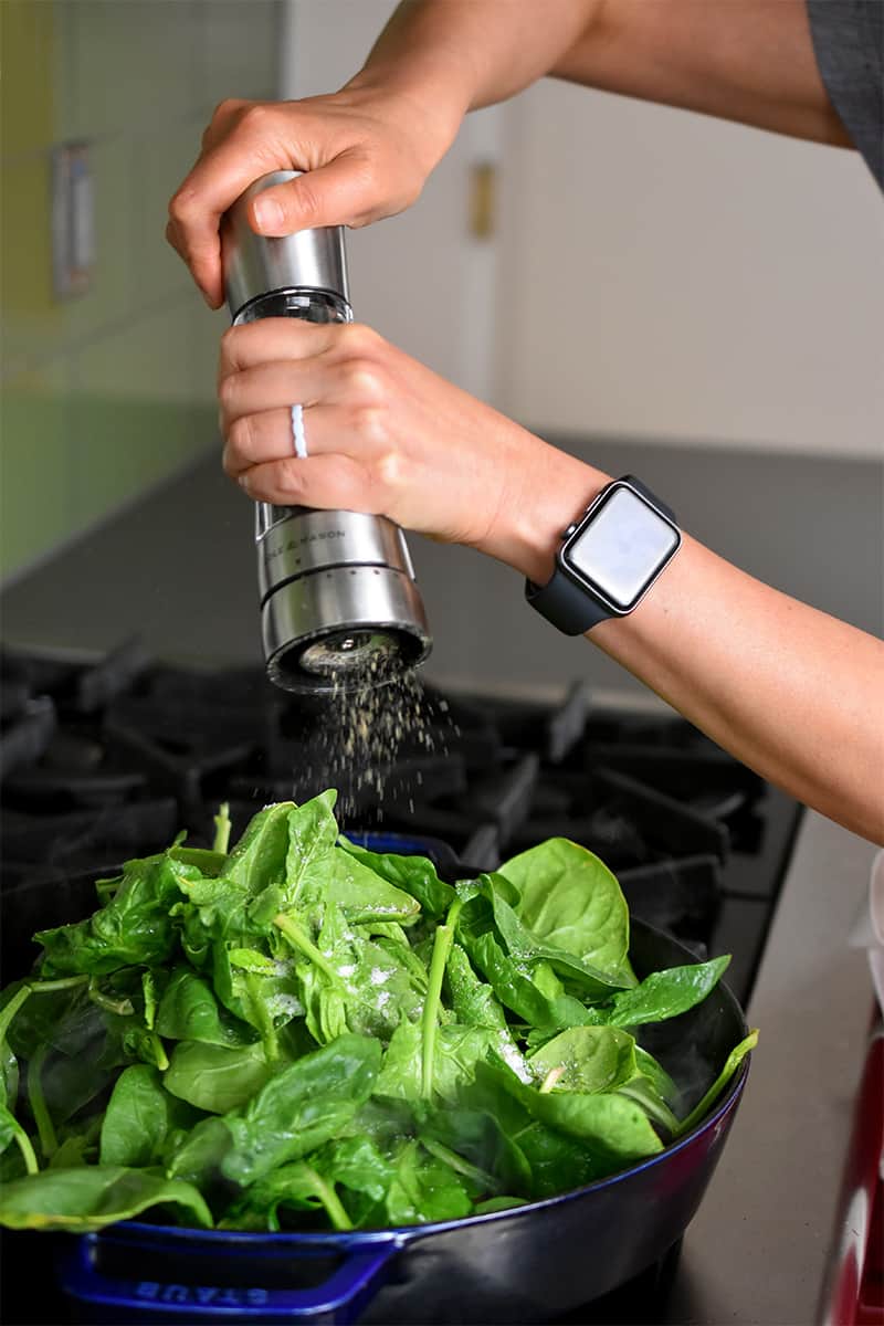 Adding pepper from a pepper mill to a skillet filled with spinach