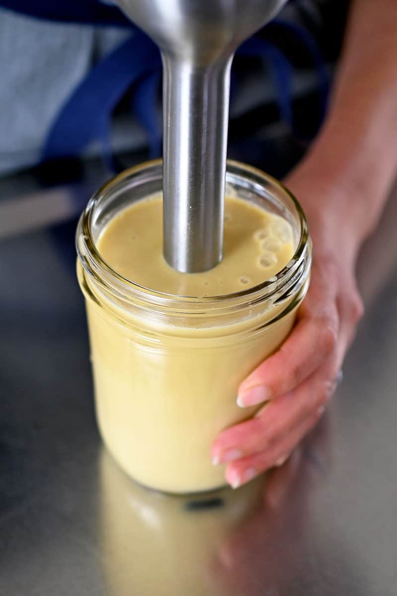Closeup view of an immersion blender mixing sesame ginger sauce in a glass jar.