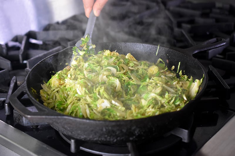 Sautéing shaved Brussels sprouts and shallots in a large cast iron skillet
