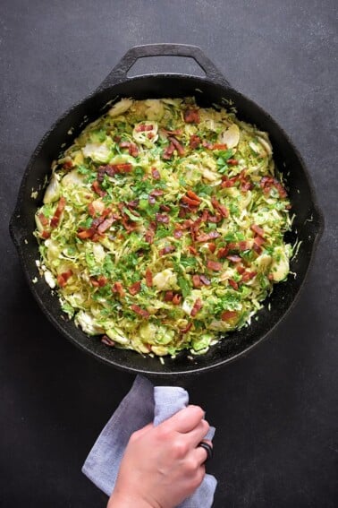 An overhead shot of shaved Brussels sprouts with bacon in a large cast iron skillet.