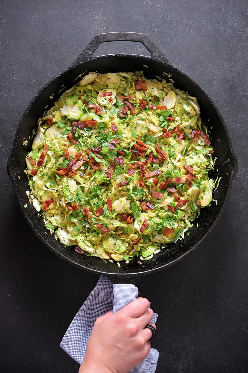 An overhead shot of a cast iron skillet filled with shaved brussels sprouts with bacon.