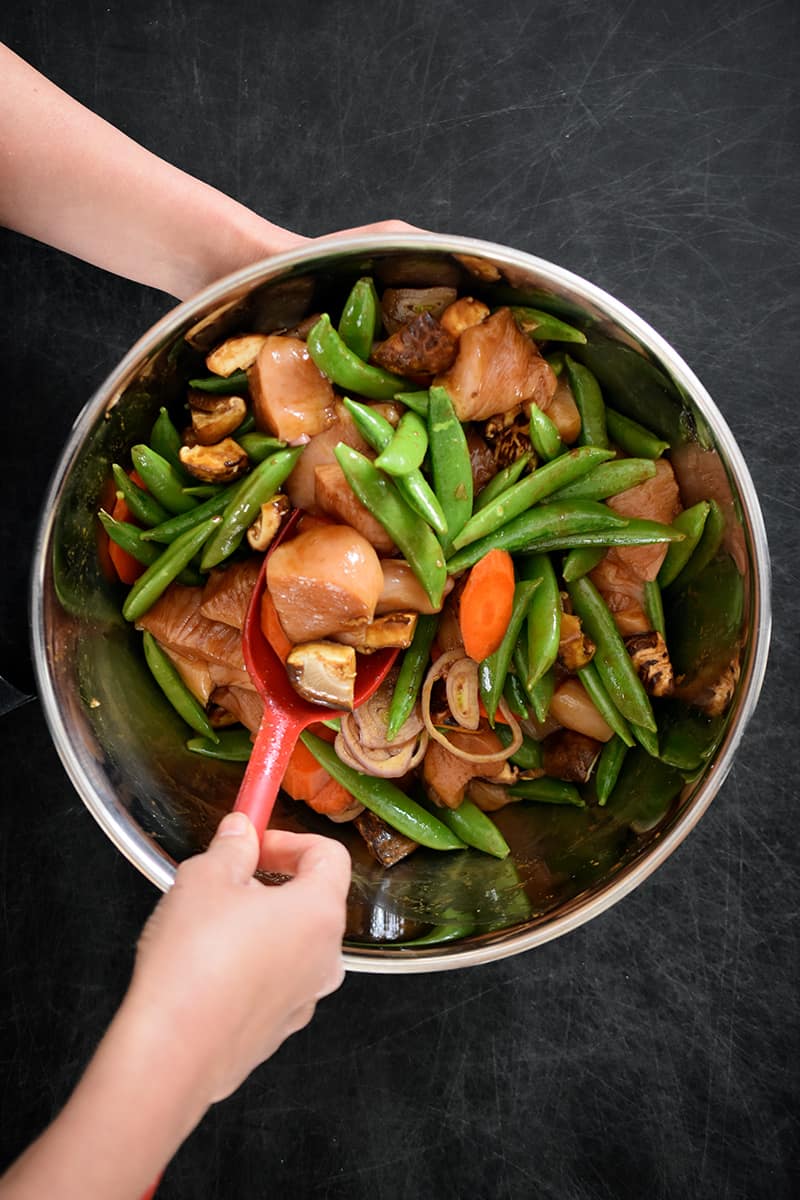 An overhead shot of someone mixing vegetables and chicken with stir-fry sauce