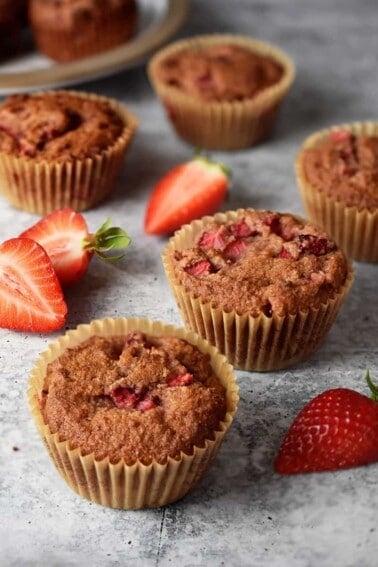 Paleo strawberry muffins on a marble countertop surrounded by sliced strawberries.