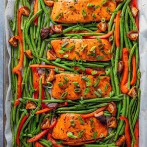 An overhead shot of Whole30 and paleo Teriyaki Salmon Sheet Pan, four cooked salmon fillets surrounded with cooked green beans and bell peppers.