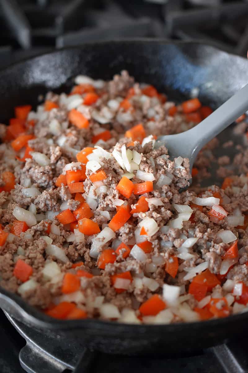 An overhead shot of a cast iron skillet filled with ground beef, diced onions, and red bell peppers. 