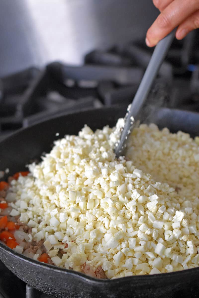 Adding cauliflower rice to a skillet to make the filling for Whole30, paleo, and low carb Tex-Mex Beef and Rice Casserole