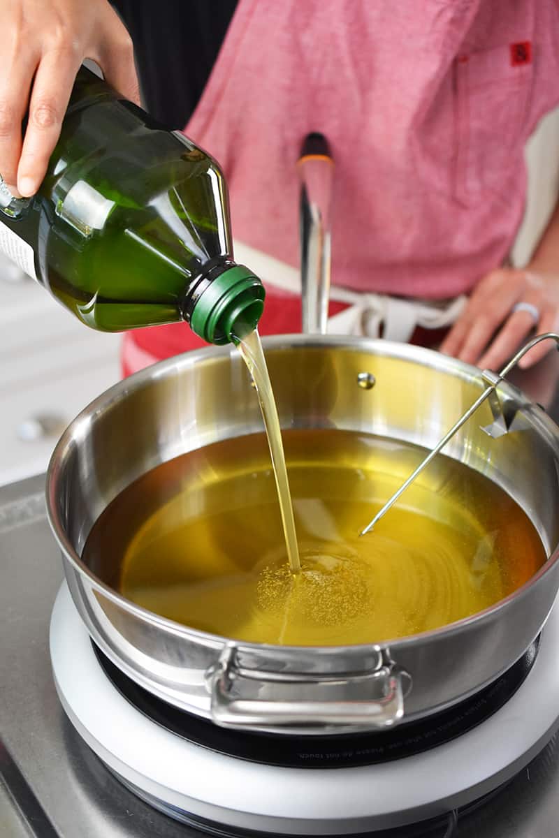 A person in a red apron is pouring avocado oil into a pot.