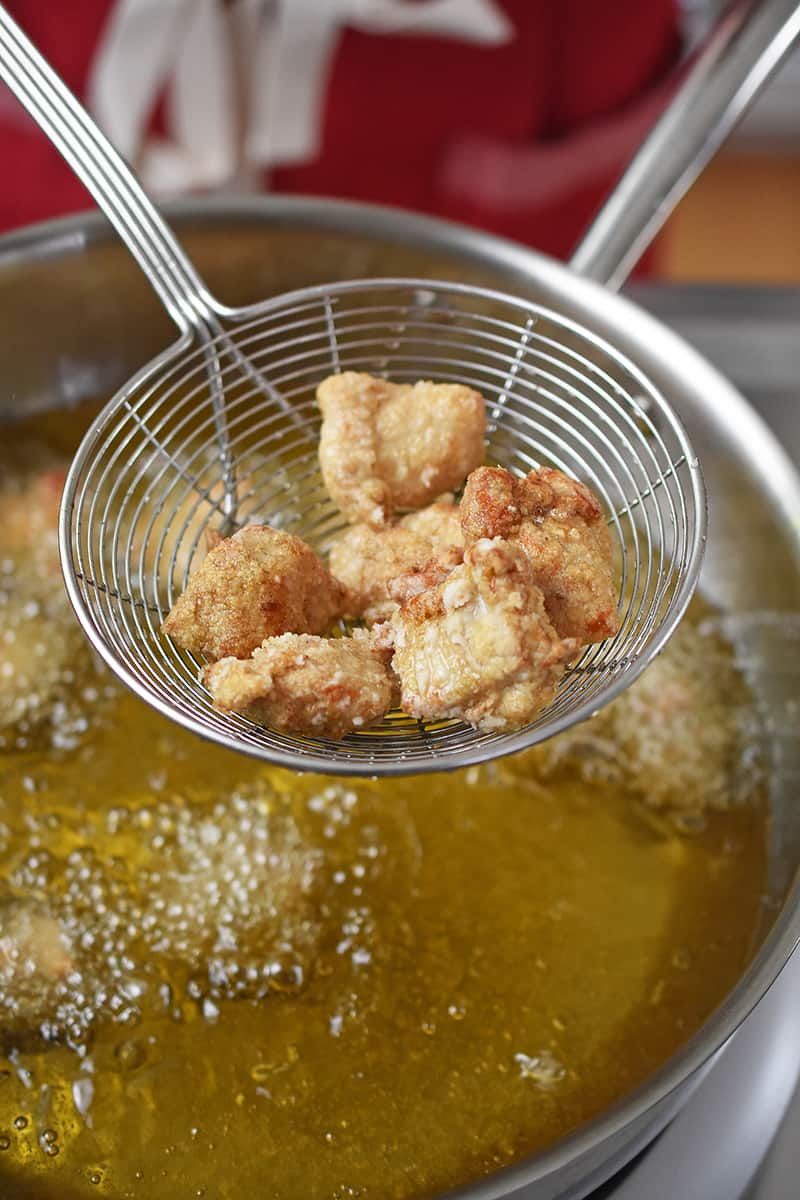 An overhead shot of a metal strainer removing Taiwanese popcorn chicken from a pot filled with hot oil.