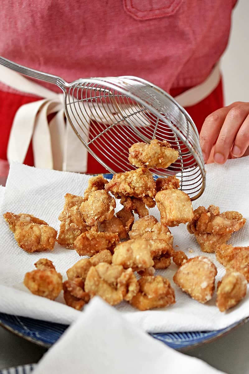 Transferring the deep fried Taiwanese fried chicken onto a paper towel lined plate.