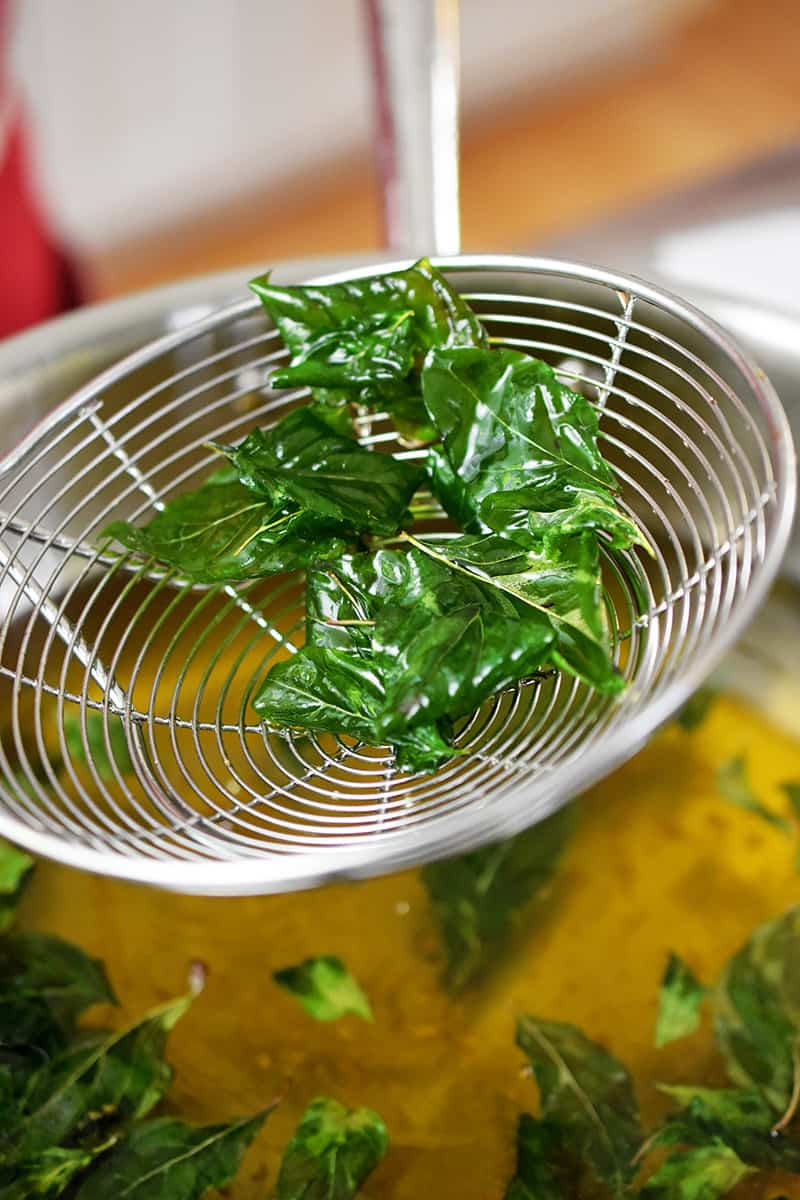 A metal strainer has fried basil in it.