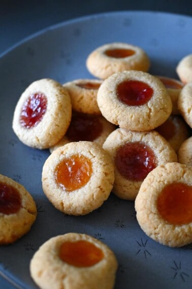 A blue plate is piled with paleo and gluten free thumbprint cookies filled with apricot and strawberry jam.
