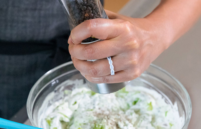 Someone adding freshly cracked pepper to a bowl of Whole30 and vegan tzatziki sauce.