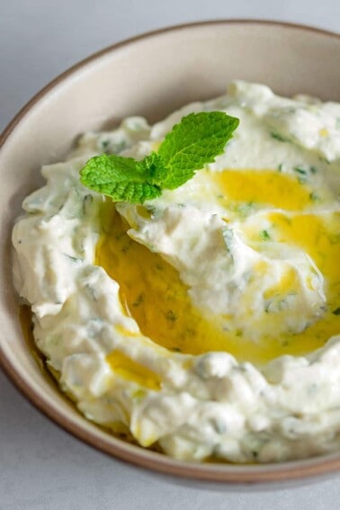 An overhead shot of keto, low carb, paleo, and Whole30 Tzatziki Sauce in a brown bowl topped with olive oil and mint.