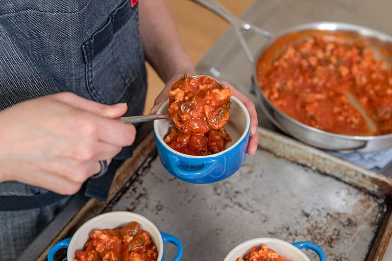 Spooning a spicy sausage and mushroom tomato sauce to make Whole30 eggs in purgatory.
