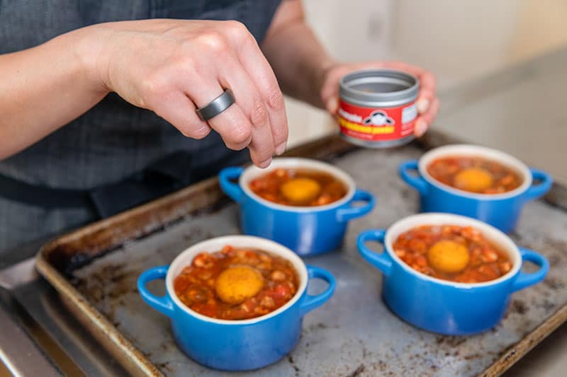 Sprinkling Nom Nom Paleo Magic Mushroom Powder on top of the Eggs In Purgatory that are going into the oven.