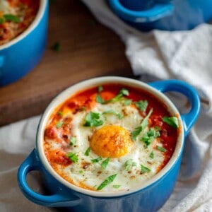 An overhead shot of three blue cocottes filled with Whole30 eggs in purgatory, baked eggs in a spicy tomato meat sauce