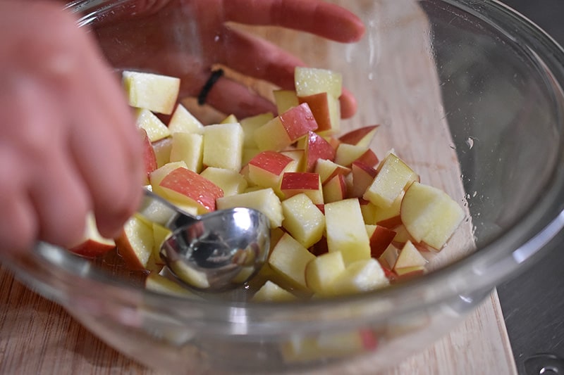 Tossing chopped apple cubes with lemon juice in a bowl with a small spoon.