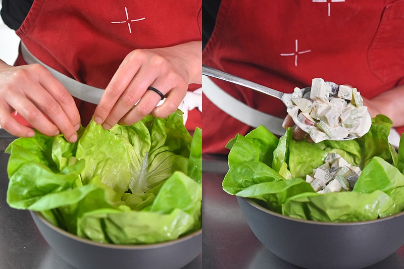 Spooning chicken waldorf salad onto a bed of lettuce leaves.