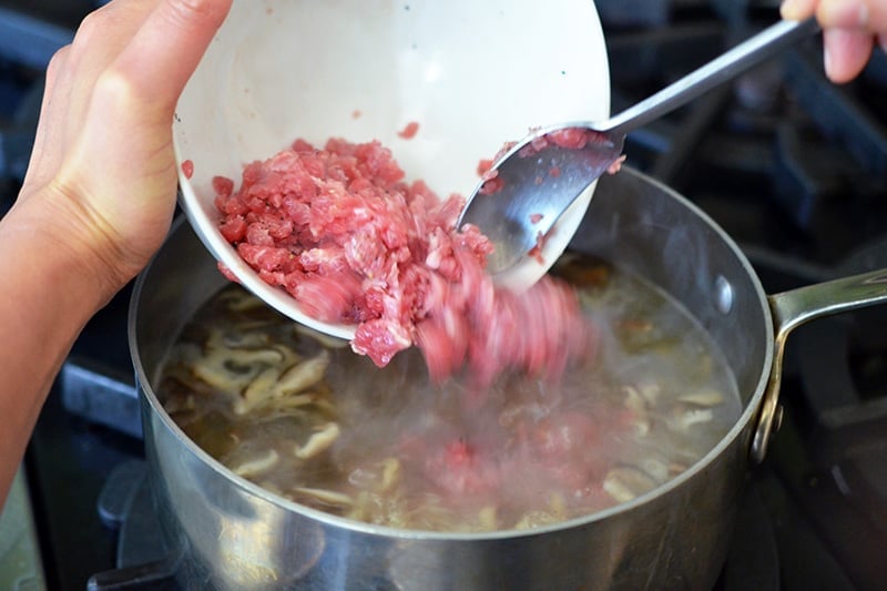Adding the seasoned minced flank steak to the simmering broth.