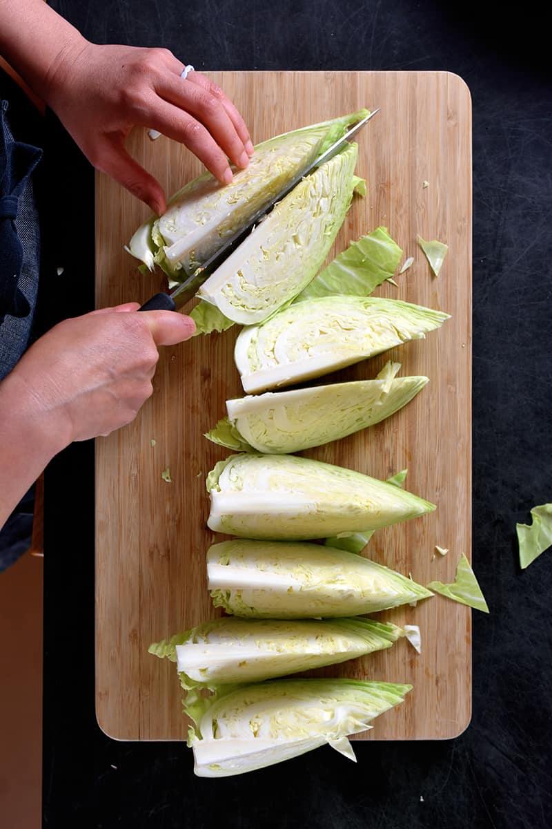 An overhead shot of someone cutting up a green cabbage into 8 wedges on a wooden cutting board