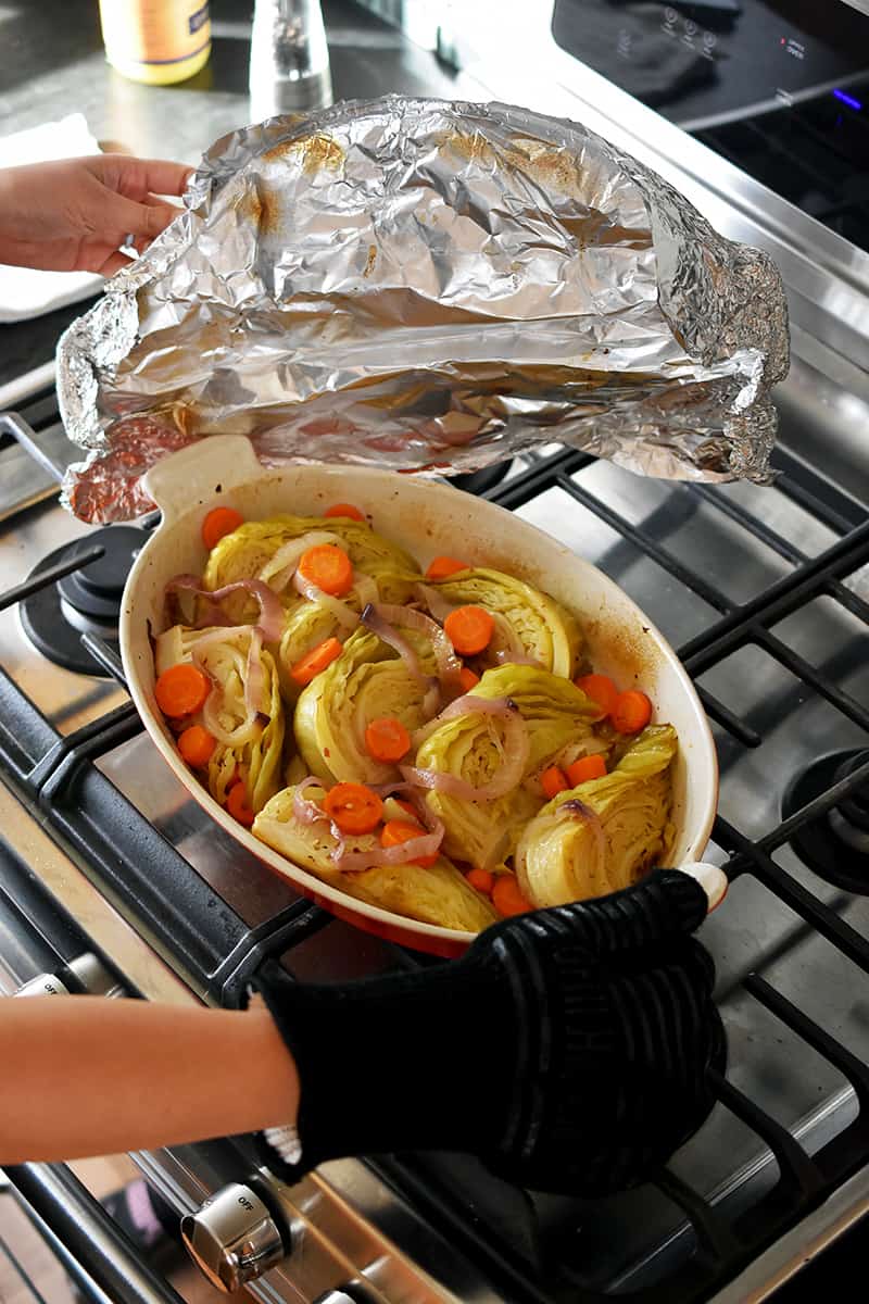 Removing foil from a casserole pan filled with braised cabbage out of the oven.