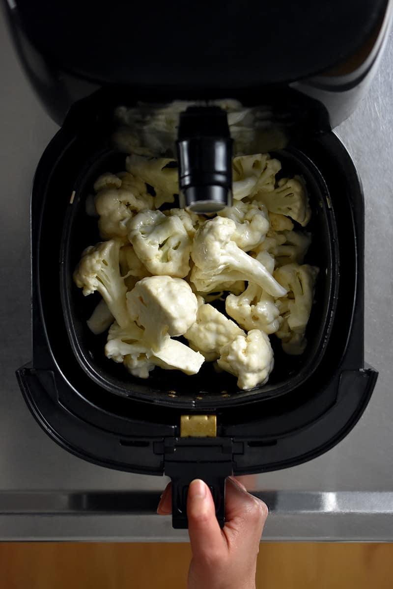 An overhead shot of Buffalo Cauliflower florets in an air fryer basket about to be cooked.