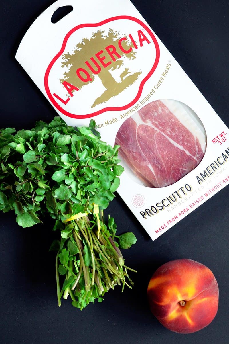 Prosciutto, watercress, and a peach sitting on a counter for the Watercress with Seared Prosciutto and Peaches recipe.