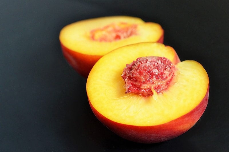 A peach sliced in half sitting on a counter.