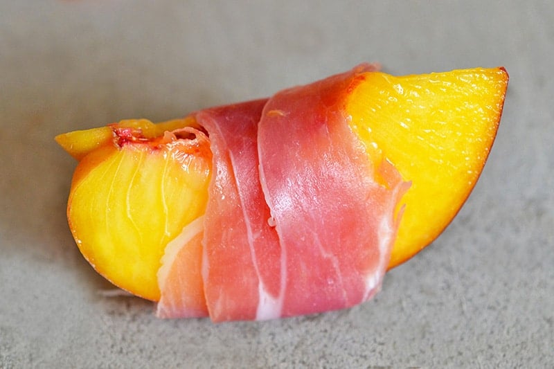 A quartered peach wrapped with a thin slice of prosciutto.