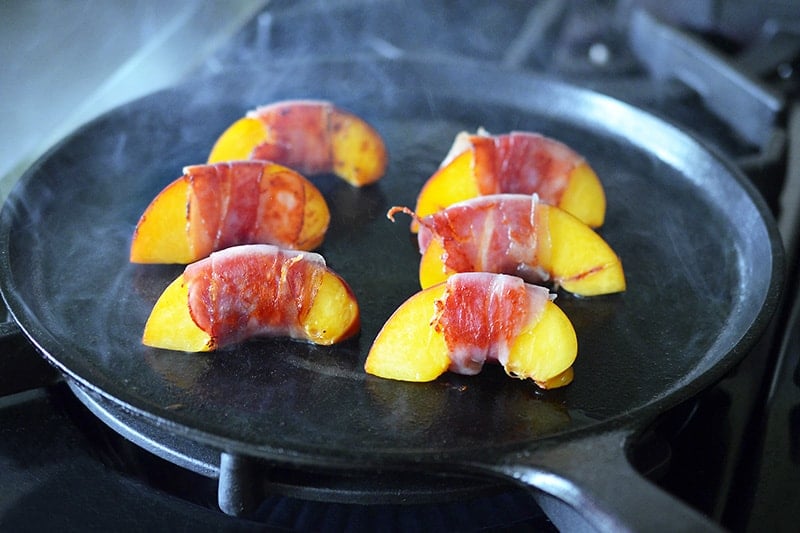 Prosciutto wrapped peaches searing on a cast iron skillet.